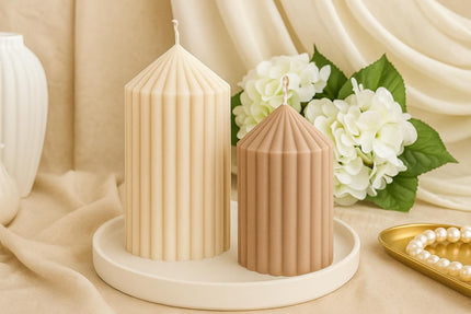 Two ribbed candles on a white plate with flowers and a pearl necklace in the background.