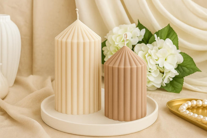 Two ribbed candles on a white plate with flowers and a pearl necklace in the background.