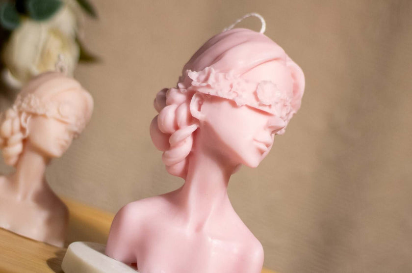 Sculptural blindfold woman candle in pink soy wax, representing grace and feminine mystery.