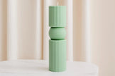 Green ribbed candle on a white surface with a neutral background