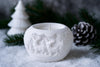 White ceramic candle holder with animal designs on a snowy background