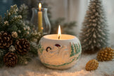 Decorative candle with festive design surrounded by pine cones and small trees