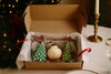 Open box containing a candle and two small green christmas tree candles on a festive background with Christmas decorations.