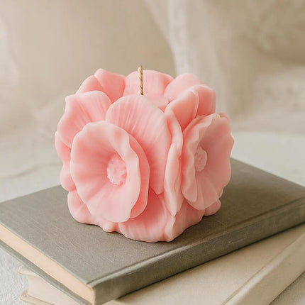 Pink flower-shaped candle on a stack of books with a soft beige background