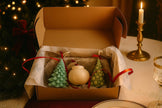 Decorative items in a box with Christmas tree ornament candles and a globe candle on a festive table.