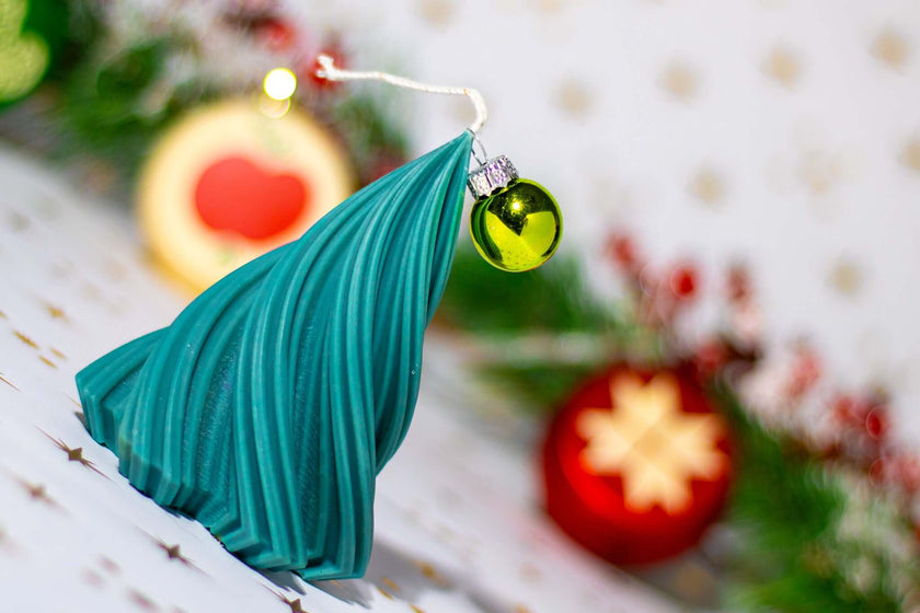 Artisan teal Christmas tree candle with a small ornament, set against festive decorations for a cozy holiday atmosphere.