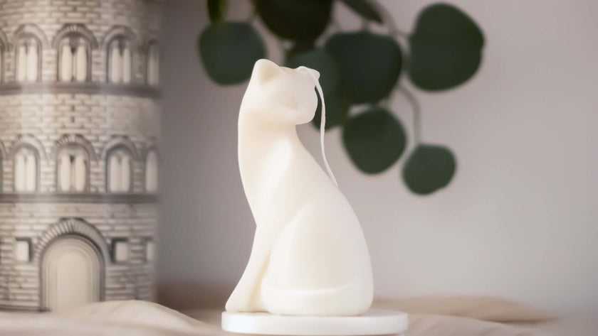 Handcrafted white cat-shaped candle beside an architectural candle holder.