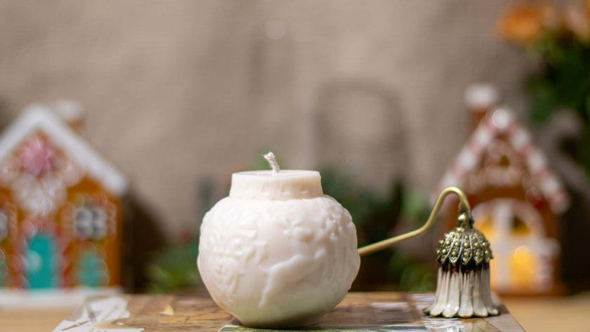 Elegant white scented candle shaped like a globe, surrounded by festive gingerbread houses, perfect for Christmas decor.