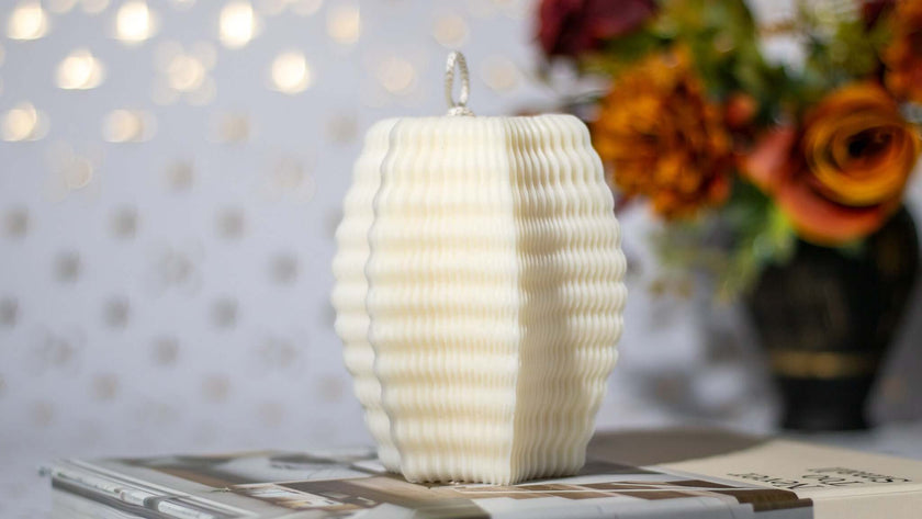 Elegant white natural scented candle with textured design, placed on a coffee table with decorative flowers in the background.