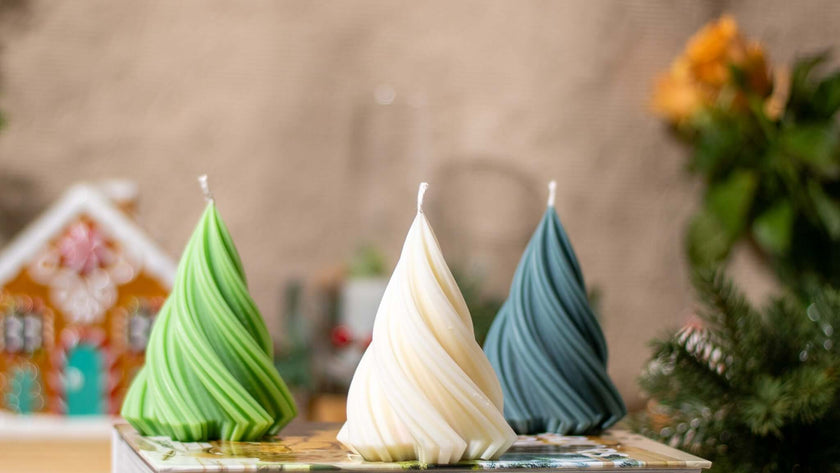 Three small Christmas tree-shaped scented candles in green, white, and gray, perfect for festive holiday decor.