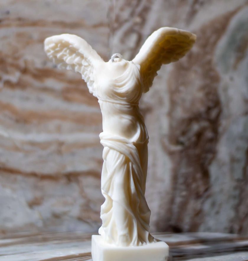 Winged Victory sculptural candle made of creamy soy wax on a marble surface.
