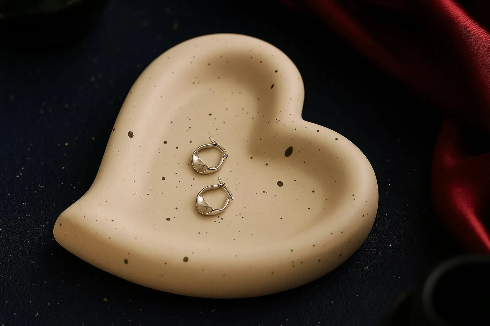 Heart-shaped ceramic dish with two silver rings on a dark surface