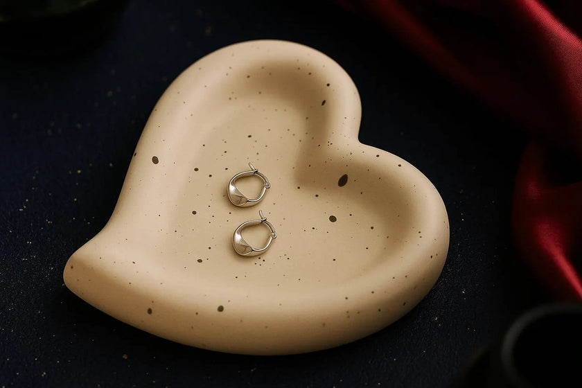 Heart-shaped ceramic dish with two silver rings on a dark surface