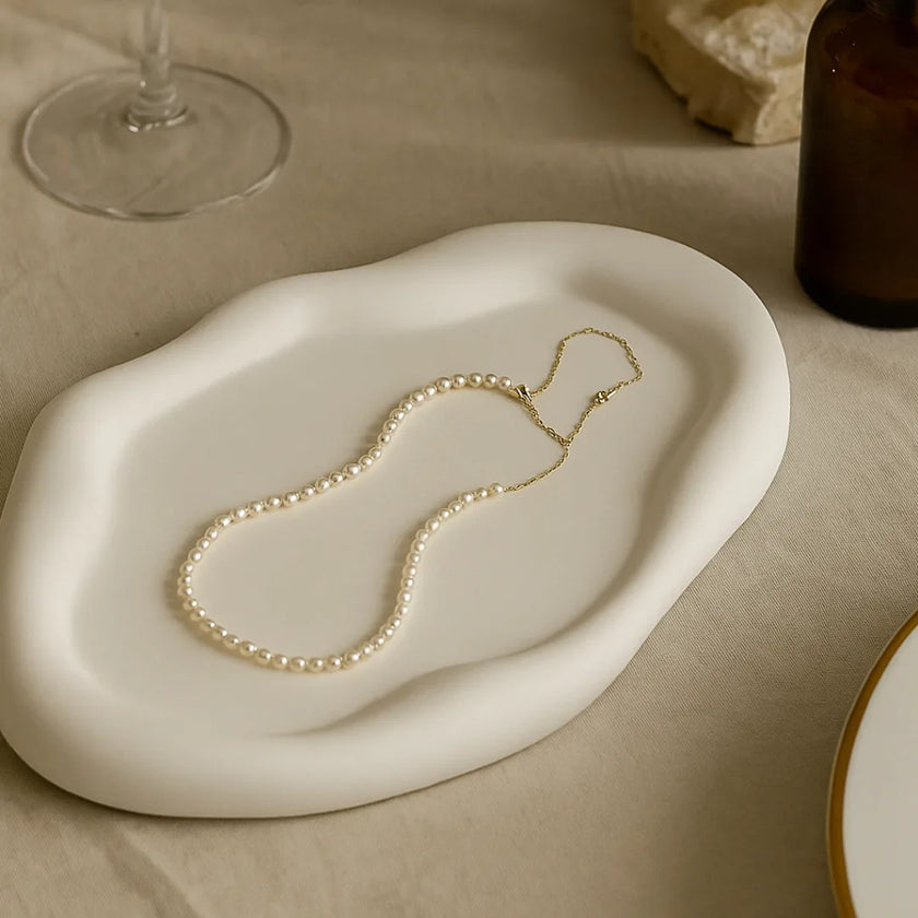 Gold necklace on a white ceramic dish with a neutral background