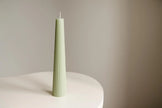 Green textured candle on a white surface with a beige background