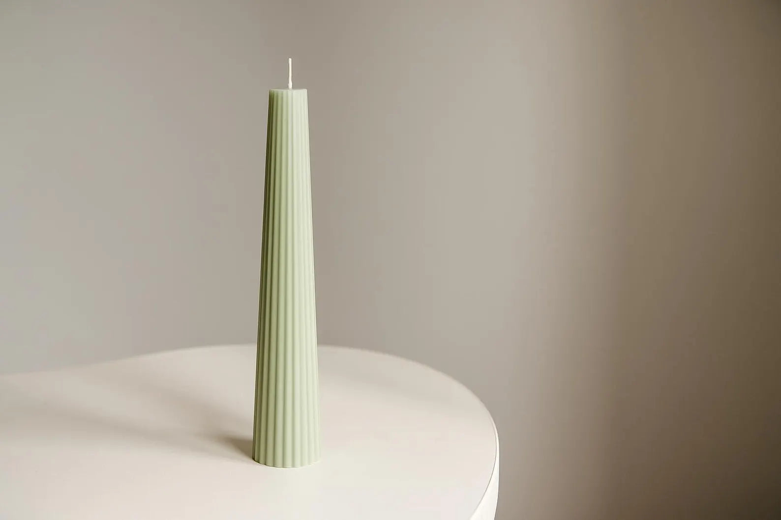 Green textured candle on a white surface with a beige background