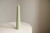 Green textured candle on a white surface with a beige background