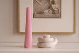 Pink candle on a white surface with a framed artwork in the background