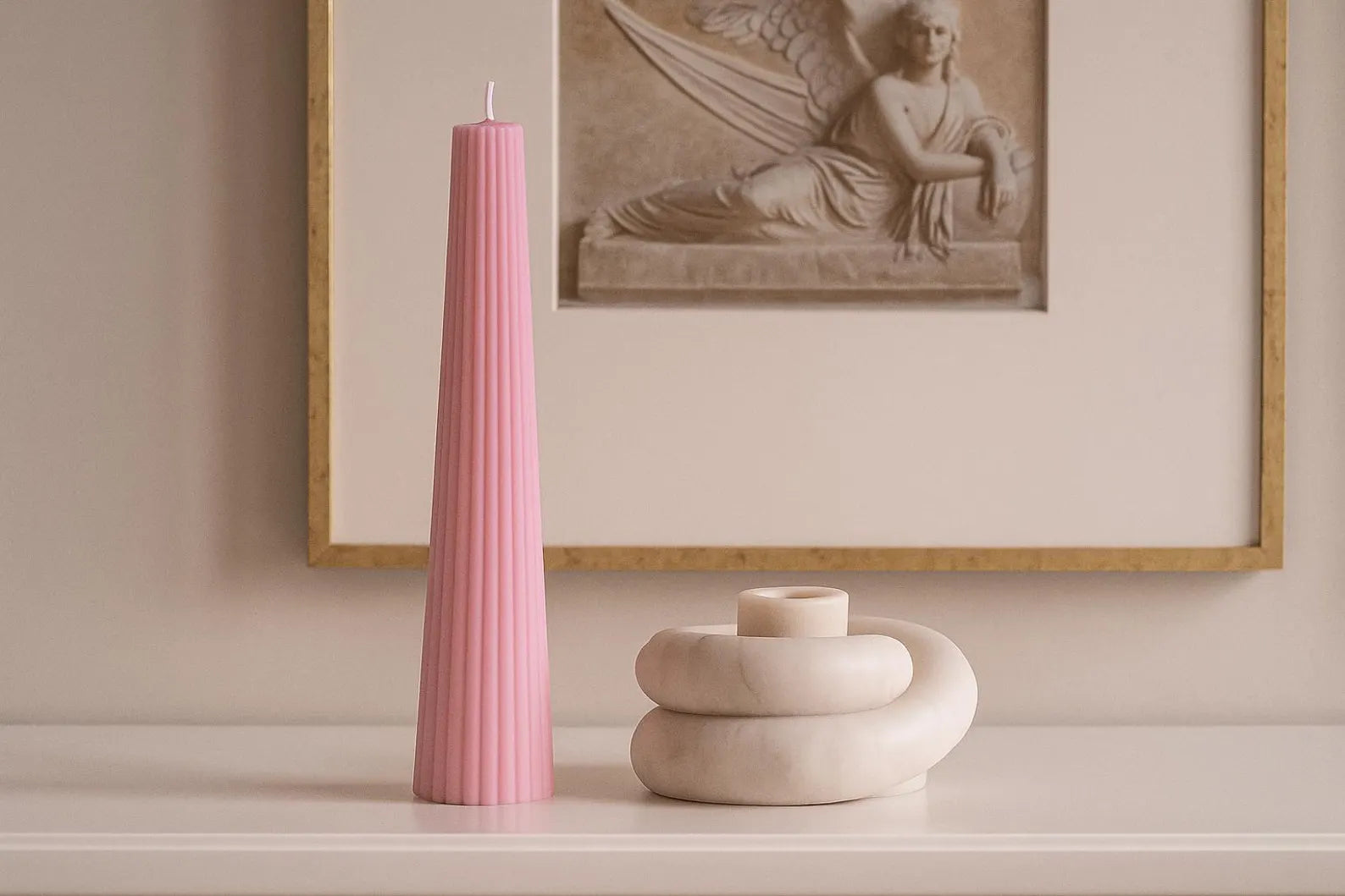 Pink candle on a white surface with a framed artwork in the background
