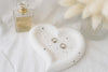 Heart-shaped ceramic dish with earrings on a white surface next to a perfume bottle.