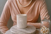 Person wearing a peach sweater with an Hermes candle on a marble surface.
