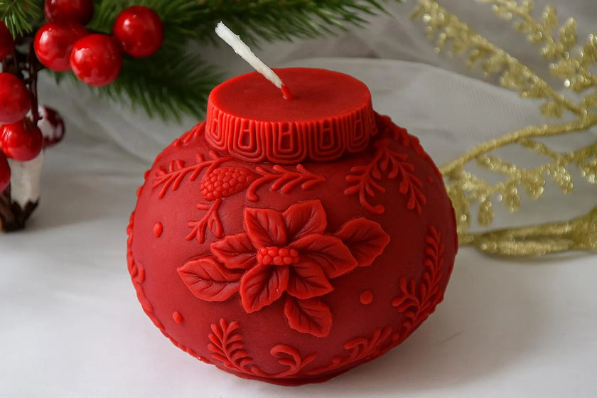 Red decorative candle with floral design on a white surface with Christmas decorations.