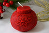 Red decorative candle with floral design on a white surface with Christmas decorations.