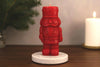 Red nutcracker-shaped candle on a wooden surface with a blurred background