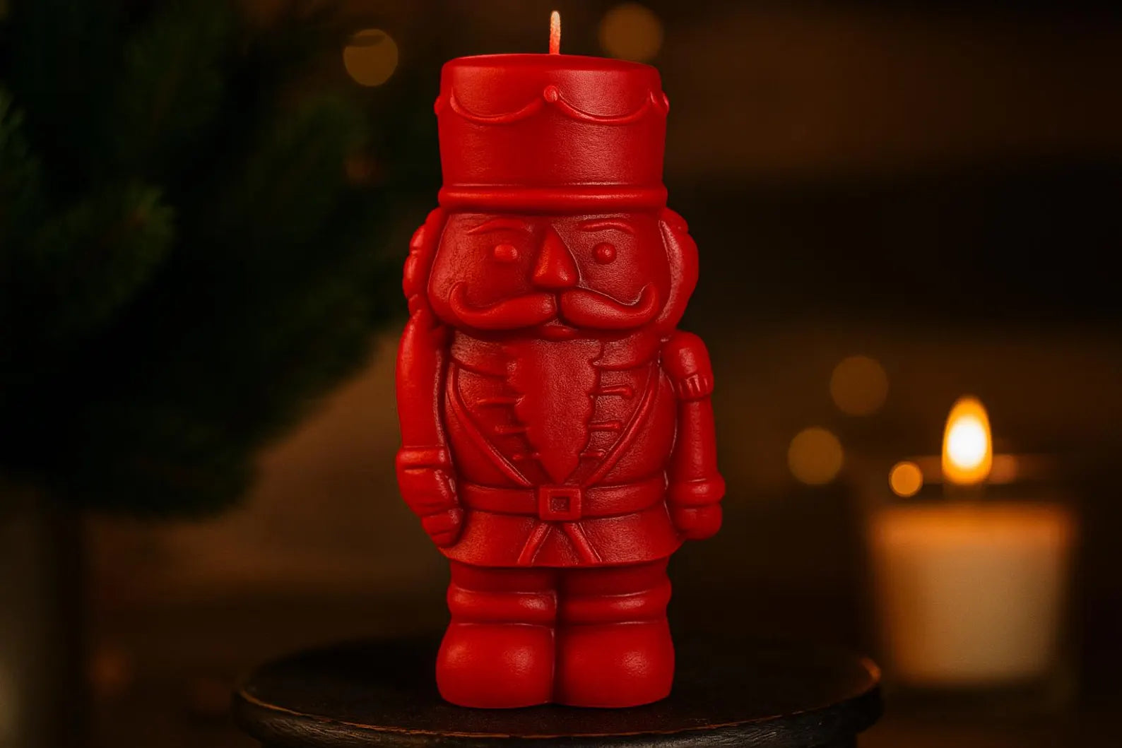 Red nutcracker candle on a dark background with another candle in the background.