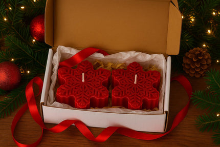 Red snowflake-shaped candles in a box with a red ribbon, surrounded by Christmas decorations.