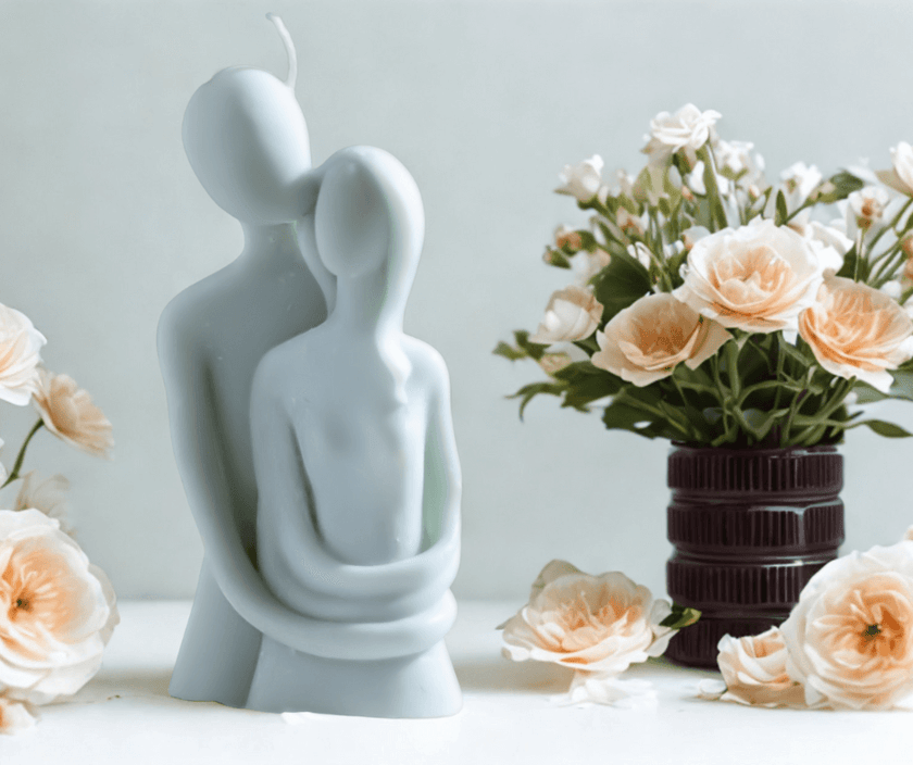 Minimalist couple embrace candle in soft pastel wax, symbolizing love and intimacy, displayed beside peach roses in a dark ceramic vase.