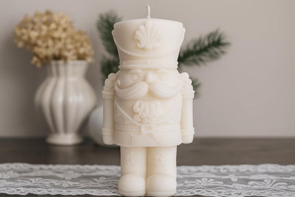 Decorative candle shaped like a nutcracker on a table with a vase and plants in the background.