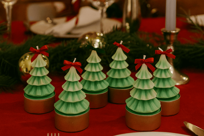 Set of Christmas tree-shaped candles on a table with a red tablecloth.