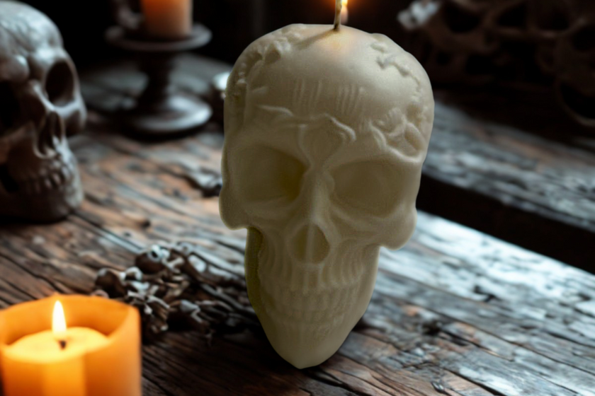 Skull-shaped candle on a wooden surface with another candle and decorative elements in the background.