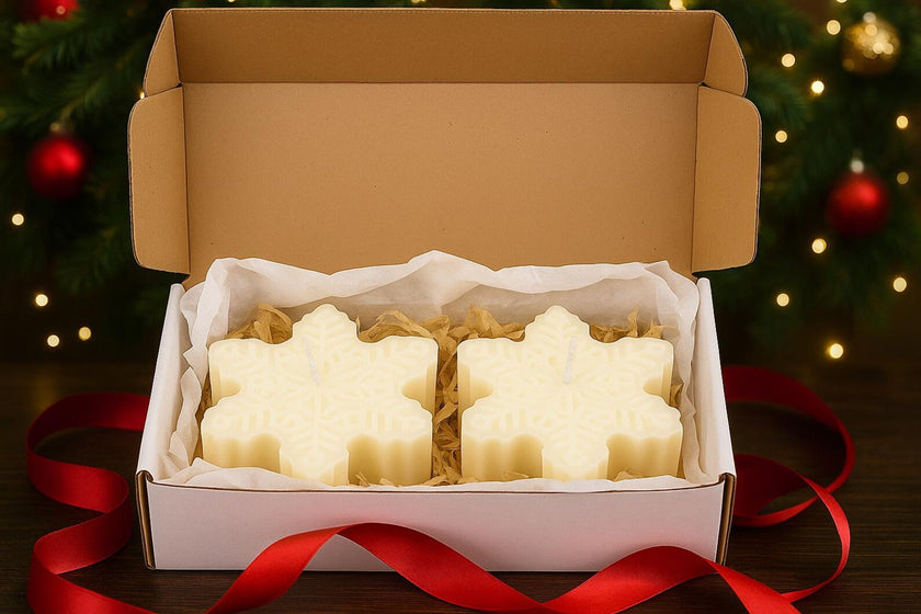 Snowflake-shaped candles in a box with a Christmas tree in the background