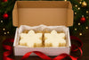 Snowflake-shaped candles in a box with a Christmas tree in the background