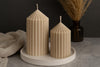 Two ribbed beige candles on a white candle holder with a dark background