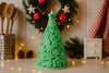 Green tree-shaped candle on a kitchen counter with festive decorations in the background