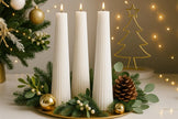 Decorative setup with white candles, greenery, and Christmas tree decorations on a table.