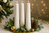 Decorative setup with white candles, greenery, and Christmas tree decorations on a table.