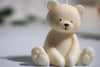 Adorable cream-colored teddy bear-shaped candle with detailed paws and a sweet smiling face, perfect for nursery or gift decor.