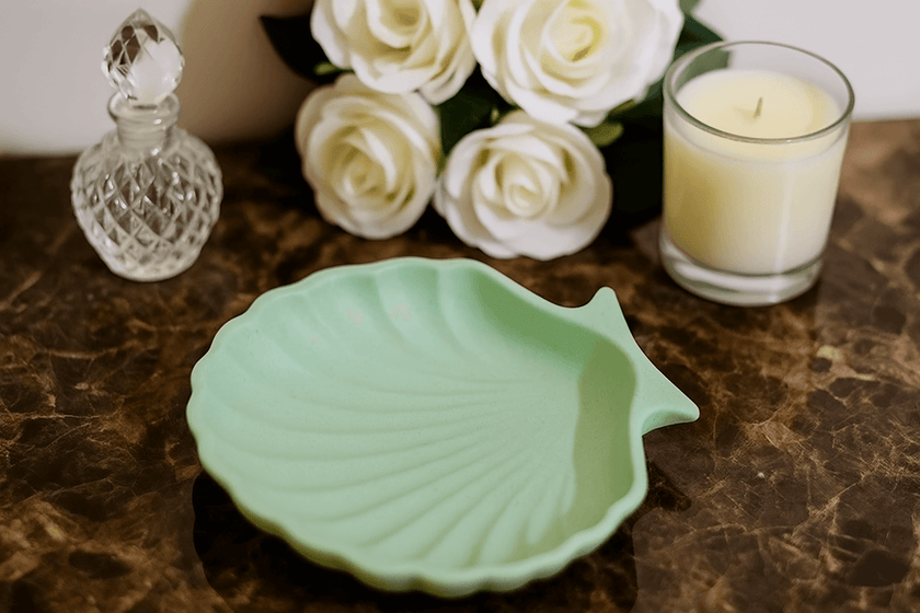 Green shell-shaped dish on a marble surface with white roses and a candle in the background.