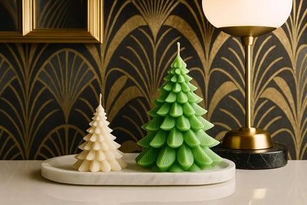 Two Christmas tree-shaped candles on a marble tray with a decorative wall in the background.