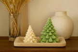 Two Christmas tree-shaped candles on a tray with decorative items in the background.