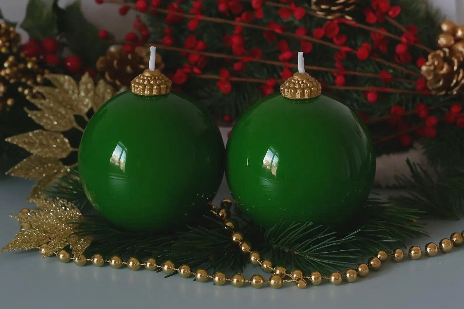Two green Christmas ornaments with gold caps on a decorative background.