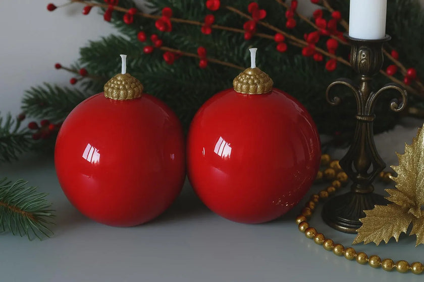 Two red Christmas ornaments with gold tops on a table with festive decorations.