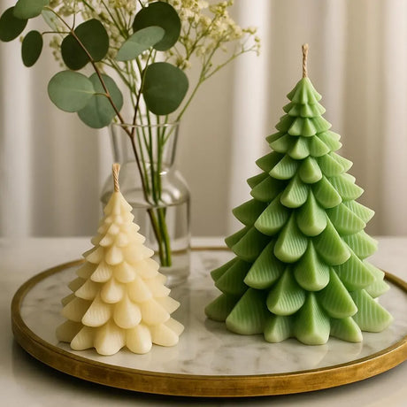 Two tree-shaped candles, one white and one green, on a marble tray with a vase of flowers in the background.