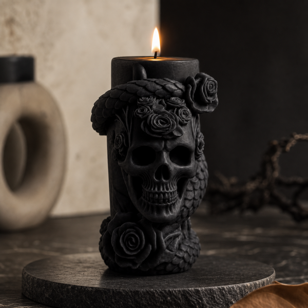 A black pillar candle with a sculpted skull and roses design, lit with a small flame, displayed on a dark stone coaster in a moody setting.