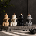 Four decorative skull candles shaped like skeletons wearing top hats and suits, arranged on a stone slab. The candles are shown in four colorways: tan, off-white, black, and gray, each with a lit flame. Halloween skeleton soy wax candle with top hat for gothic decor