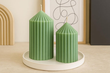 Two green ribbed candles on a white round tray with a minimal background